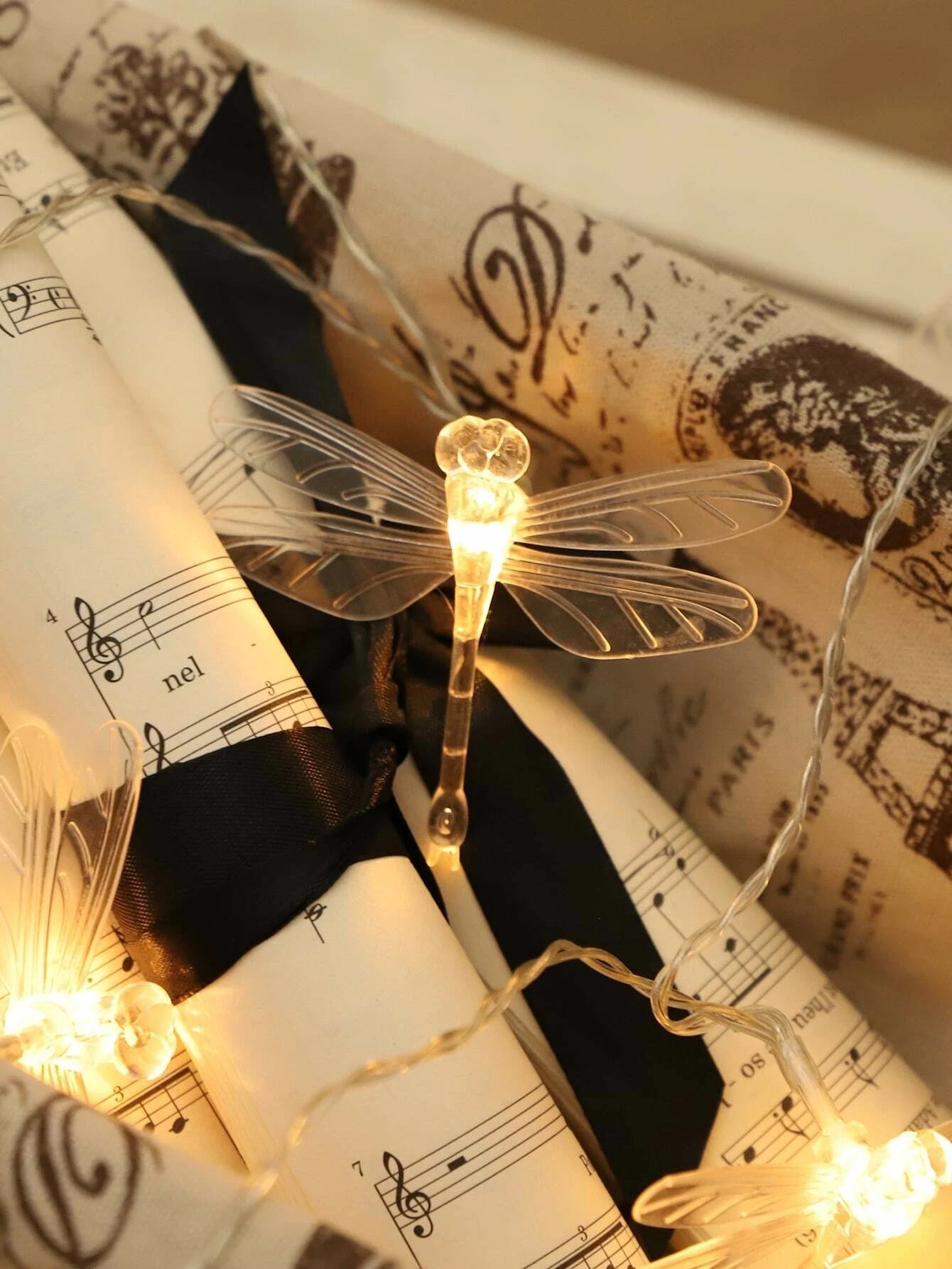 Decorative string lights shaped like dragonflies on vintage music sheet paper.