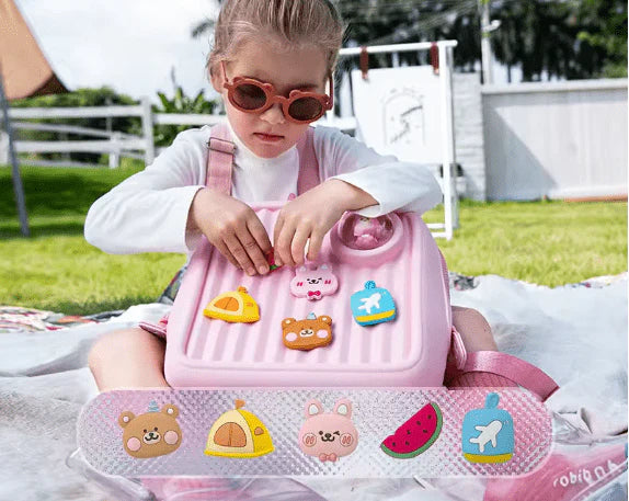 Child sitting on a pink Kids Travel Backpack with various animal stickers outdoors