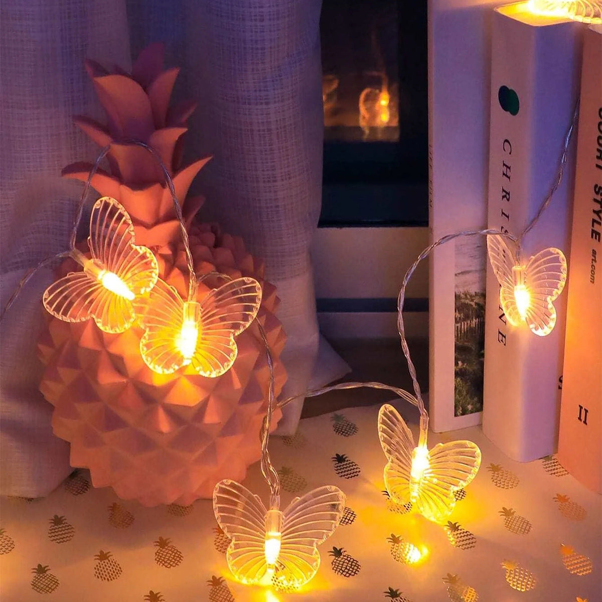 Butterfly string lights on a pineapple with books and a plant in the background