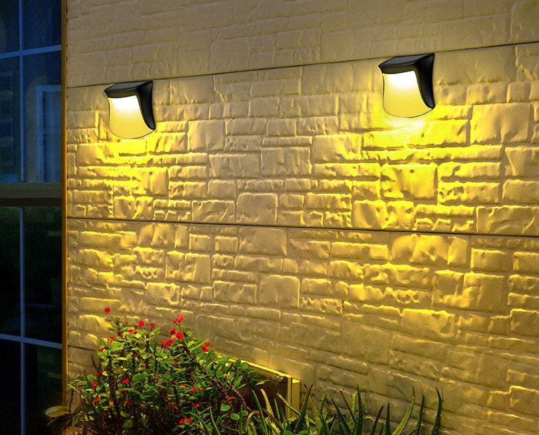 Two "4pcs Solar Lamp Fence Wall Lamp Outdoor Waterproof Home Decoration Lighting Garden Wall Lamp" on a textured brick wall with plants at the base.