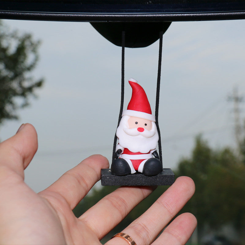 Hand holding a small Christmas Car Rearview Mirror Pendant Santa Claus figurine hanging from a string against a blurred outdoor background.