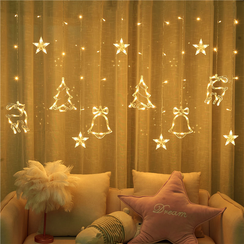 Decorative string lights with Christmas-themed decorations on a curtain, with a cozy living room setting.