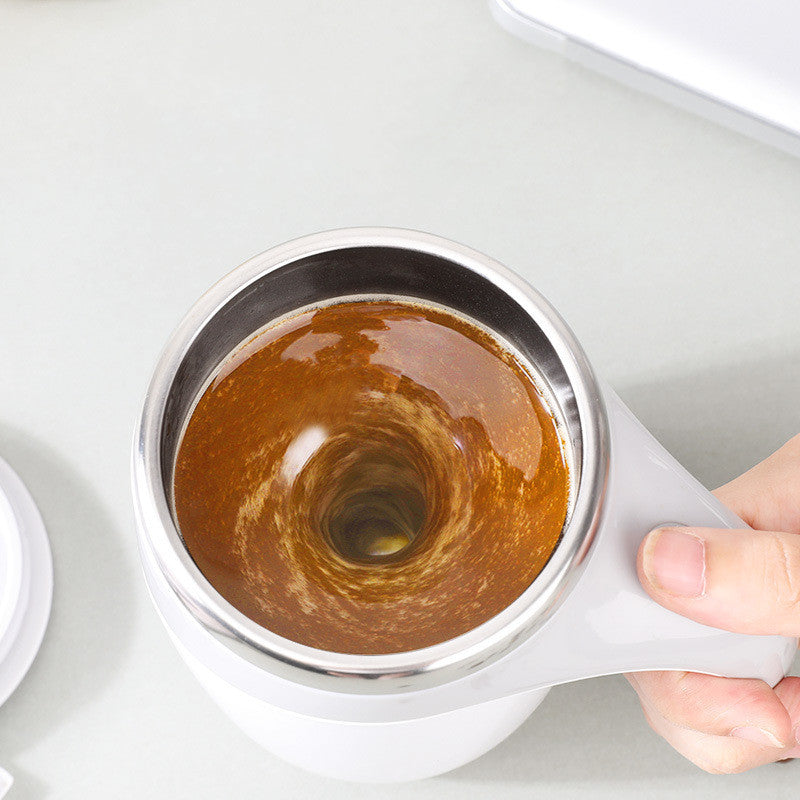 White Electric Stirring Cup Full-automatic Magnetic Rotating Coffee Mug with brown coffee grounds held by a hand on a light gray background