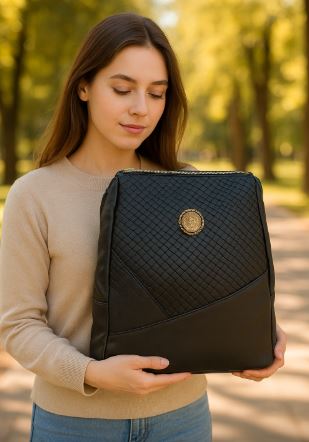 Woman holding a black Elegant Faux-Leather Backpack with a gold emblem in a park setting