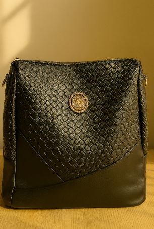 Black woven Elegant Faux-Leather Backpack with a gold emblem on a wooden surface