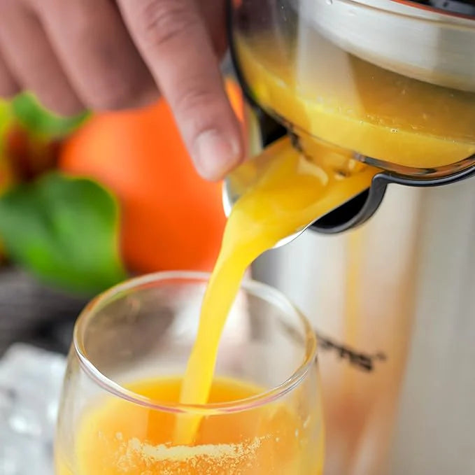 Orange juice being squeezed from a Nikai - Stainless Steel Citrus Juicer into a glass with a blurred background