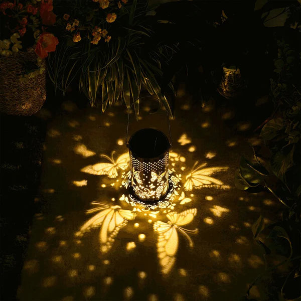 Outdoor Pluggable Or Hanging Iron Solar Butterfly Projector Lamp casting shadows on a dark surface with plants in the background