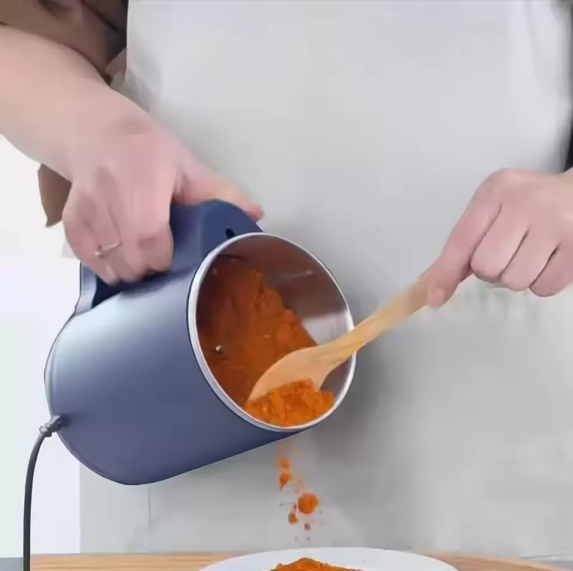 Person using a blue Electric Grinder for Coffee & beans to pour ground coffee into a bowl with a wooden spoon.