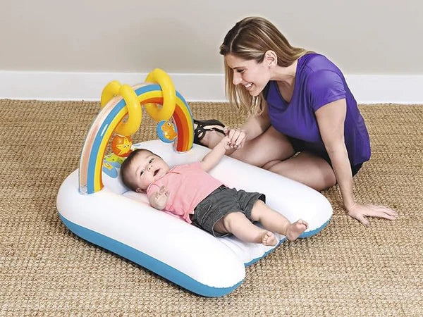 Baby lying on an Inflatable Baby Play Mat & Lounger with Rainbow Arch with a colorful toy, being played with by a woman.