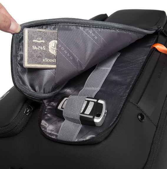 Close-up of a black "casual carry bag" backpack with a gray interior pocket and a strap, featuring a brand label.