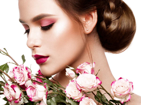 Woman with pink makeup, daisy-rose ultra smooth lipstick and braided hair holding pink roses against a white background