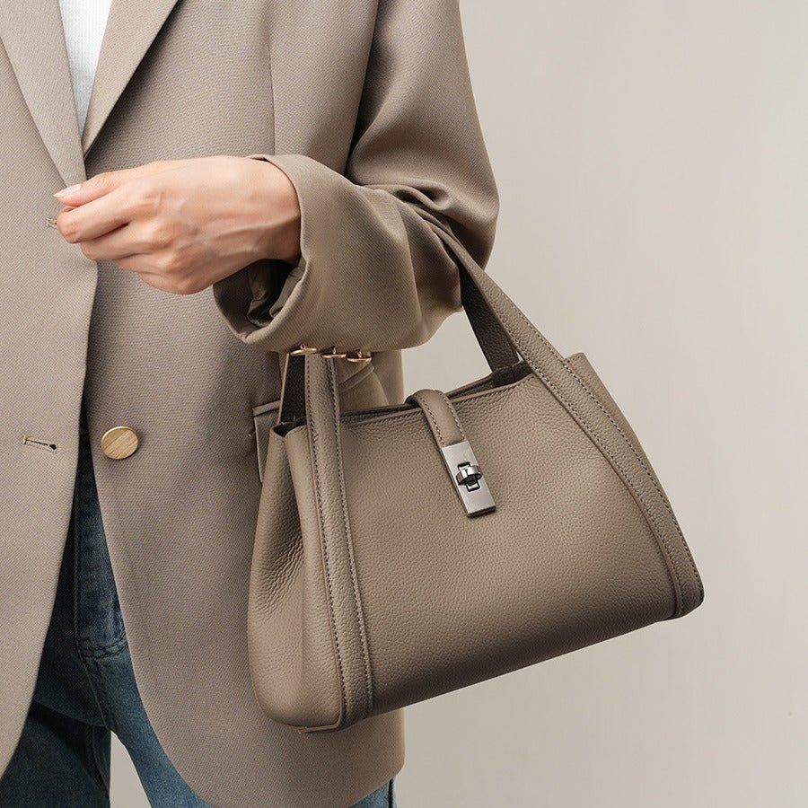Person holding a beige fashionable Korean style large capacity leather handbag with a neutral background