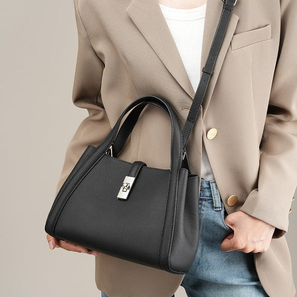 Person holding a black fashionable Korean style large capacity leather handbag wearing a beige blazer and blue jeans on a neutral background