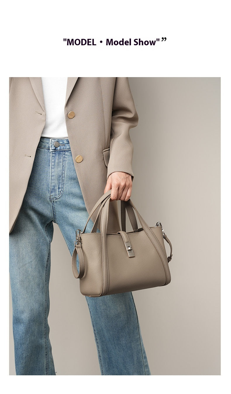 Person wearing a beige coat and blue jeans holding a beige color fashionable style large capacity  handbag against a neutral background