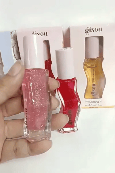 Hand holding a pink gisou honey infused lip oil bottle with gisou packaging in the background