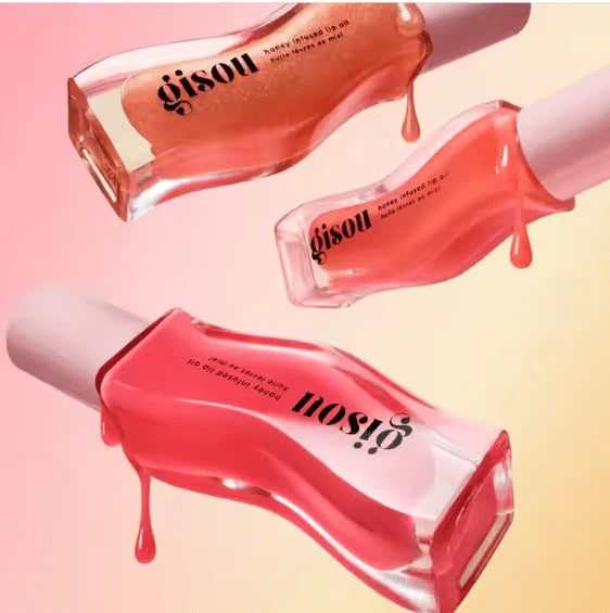 Three bottles of gisou honey lip oil product on a gradient pink and yellow background