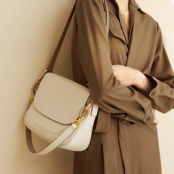 Person wearing a beige trench coat holding a high grade cowhide underarm handbag against a neutral background