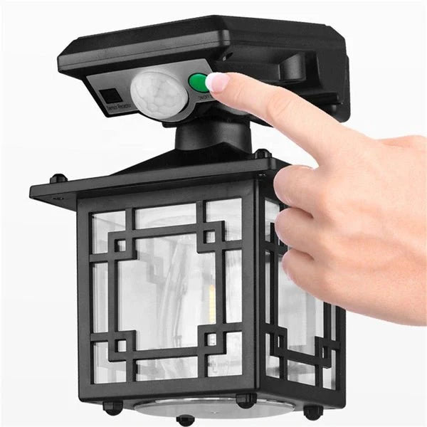 Hand pressing a button on a black  Outdoor Solar Sensor Light fixture with motion sensor